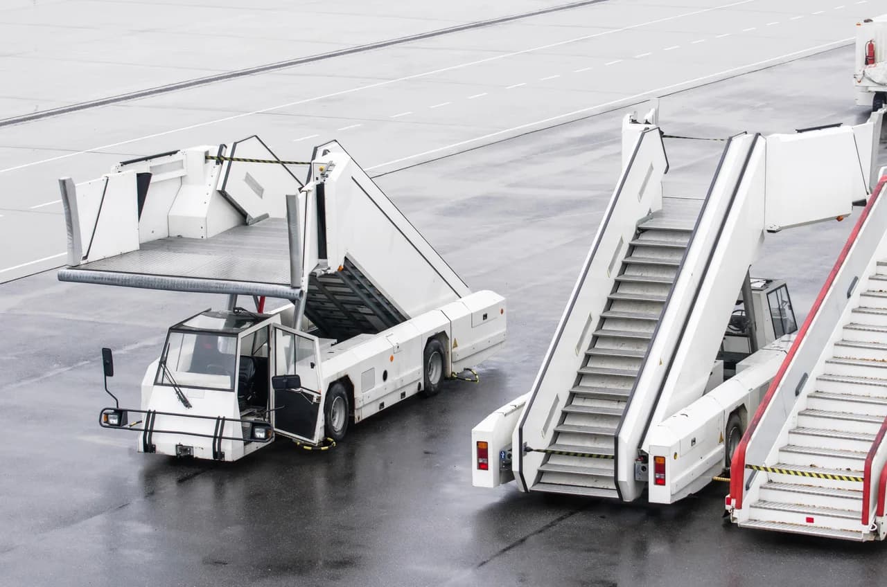 Aircraft passenger boarding stairs and ground service vehicles parked on the apron at an airport
