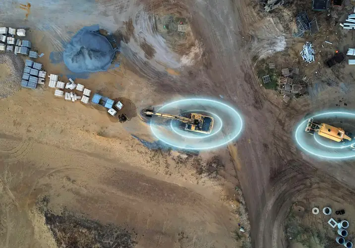 A civil site from the air: a tracked excavator and a wheel loader at work, with pallets and pipes stacked nearby